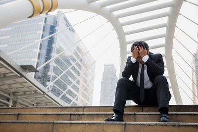 Low angle view of tensed businessman with head in hands sitting on steps in city