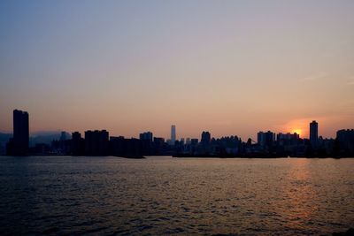 Sea by cityscape against sky during sunset
