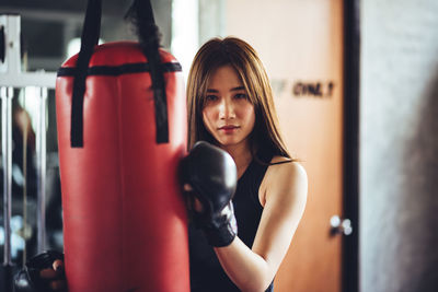 Portrait of confident young woman holding punching bag while standing in gym