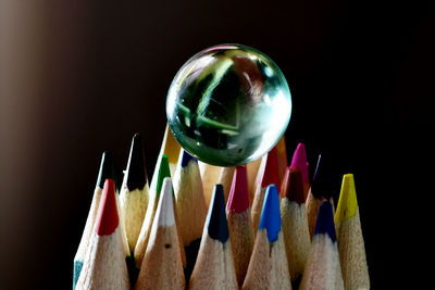 Close-up of crystal ball over multi colored pencils against black background