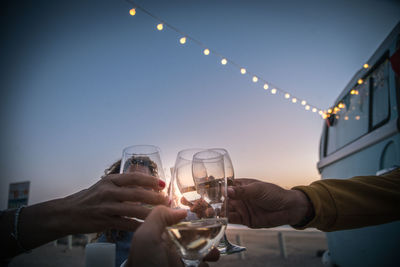 Cropped hands toasting wine outdoors during sunset