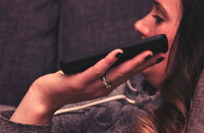 Woman holding mobile phone while lying down on sofa at home