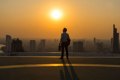 Rear view of man walking on road against sky during sunset