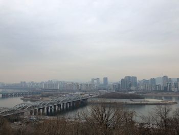 Bridge over river by buildings in city against sky