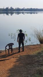 Rear view of man standing by lake against sky