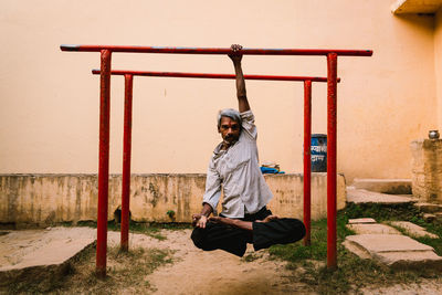 Full length portrait of young man sitting on wall