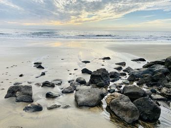 Rocks on beach against sky during sunset