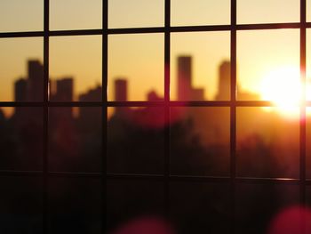 Silhouette buildings seen through glass window during sunset