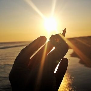 Silhouette hand on beach against sky during sunset