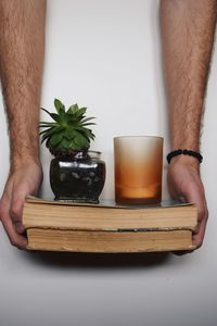 Cropped hands of man holding books with houseplant and drinking glass on wall