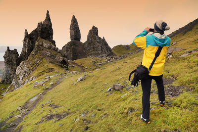 Rear view of man photographing old man of storr against sky during sunset