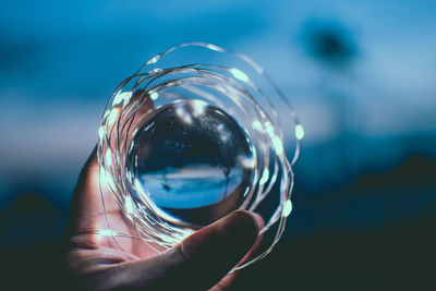 Close-up of hand holding illuminated string light amidst crystal ball