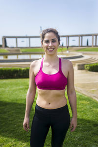 Portrait of smiling female athlete standing on grassy field against sky at park