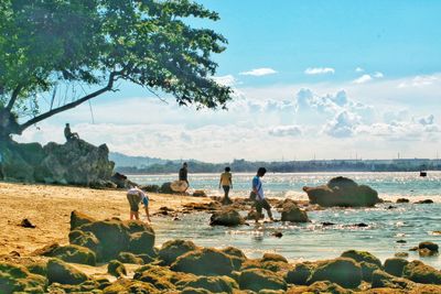 People on rocks by sea against sky