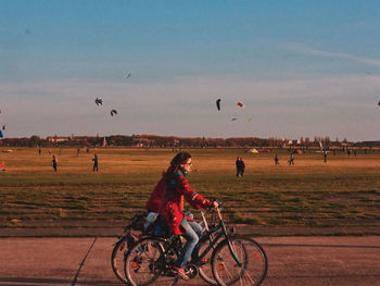 People riding bicycle on field against sky