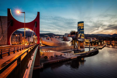 Boats moored in river against illuminated city at dusk