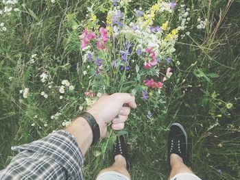 Low section of person standing by flowering plants on field