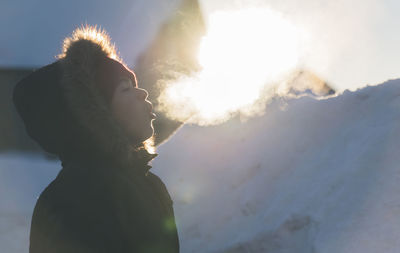 Side view of boy wearing fur coat while exhaling breath vapor during winter