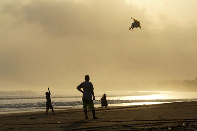 Silhouette friends flying over beach against sky during sunset