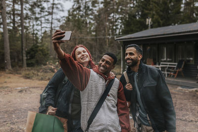 Happy friends taking selfie with mobile phone in yard