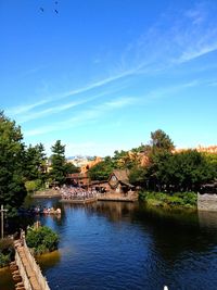 Scenic view of river by building and trees against blue sky