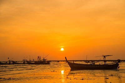 Silhouette boats moored on sea against orange sky