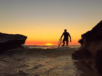 Silhouette man with surfboard on beach at sunset