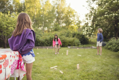 Girl looking at sister playing with friend grass in back yard