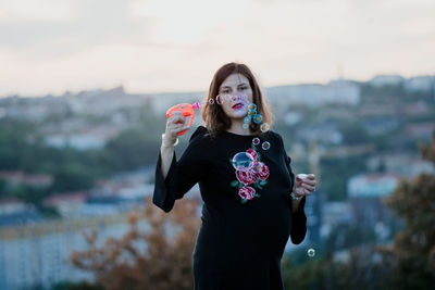 Portrait of woman holding bubble wand while standing outdoors