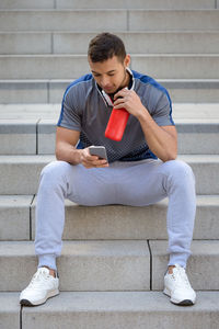 Full length of young man using mobile phone while sitting on staircase