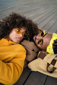 Top view of trendy african american man and woman in bright coat lying down on wooden floor looking at each other