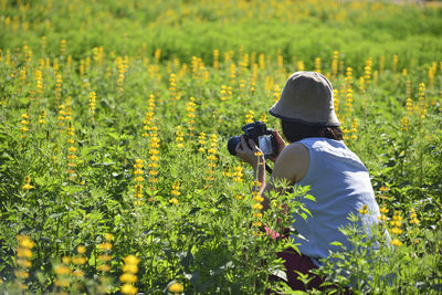 Side view of woman photographing while crouching amidst plants