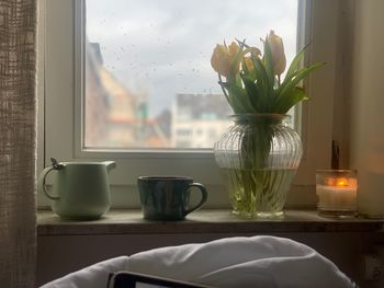 Flowers in vase with cup on window sill at home