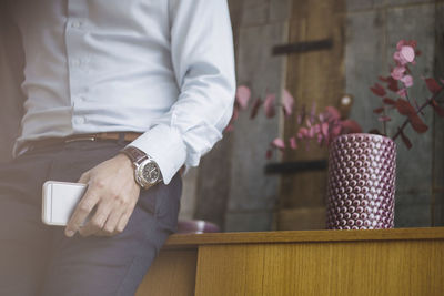 Midsection of businessman holding mobile phone while leaning on sideboard in portable office truck