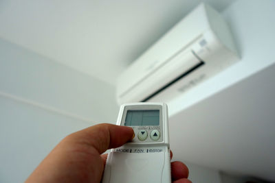 Close-up cropped hand using remote control of air conditioner