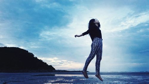 Woman jumping at beach against sky