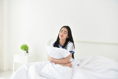 Young woman with pillow sleeping against wall on bed at home