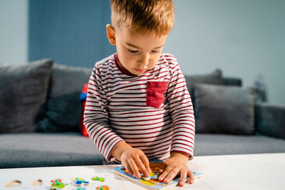 Cute boy playing with puzzle by table at home