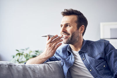 Smiling man sitting on sofa using cell phone