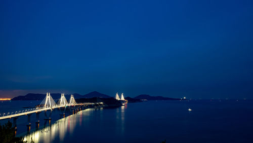 Illuminated bridge over sea against sky at dusk