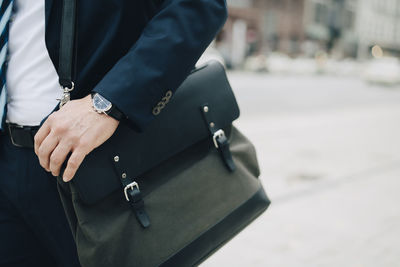 Midsection of businessman with bag standing in city