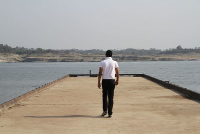 Rear view of man walking on pier against clear sky