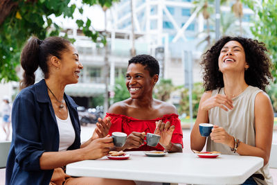 Smiling friends using mobile phone while sitting in cafe