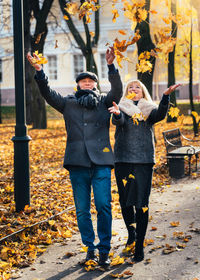 Couple throwing autumn leaves in mid-air at city