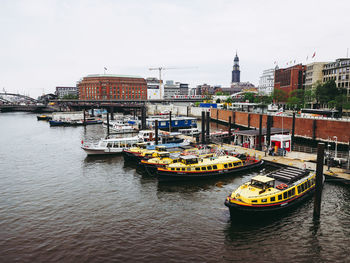 Boats in river by buildings in city against sky