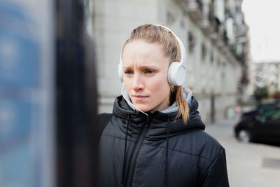 Young woman listening to music using parking meter in city