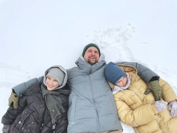 Low angle view of father with two kids lying on snow covered landscape