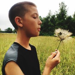 Close-up of boy blowing flower while standing by plants