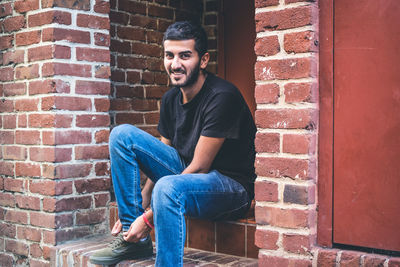 Portrait of young man sitting against brick wall