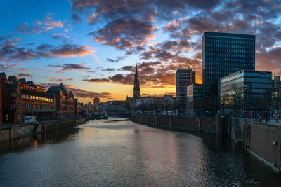 Buildings by river against cloudy sky